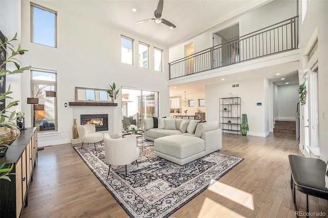 living area with a glass covered fireplace, wood-type flooring, ceiling fan, and baseboards