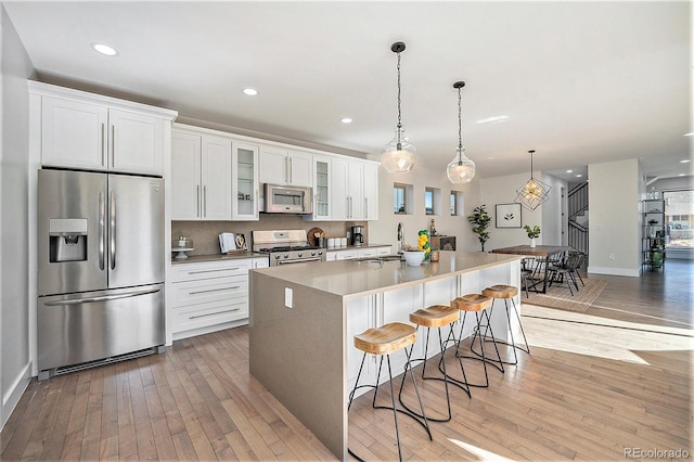 kitchen featuring stainless steel appliances, white cabinets, light wood-style floors, and an island with sink