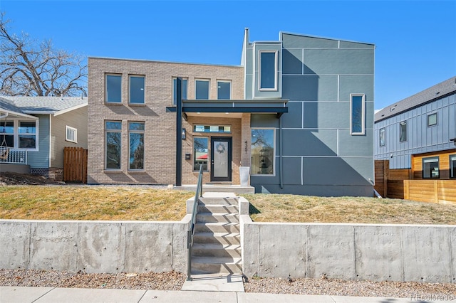 modern home with brick siding, a front lawn, and fence