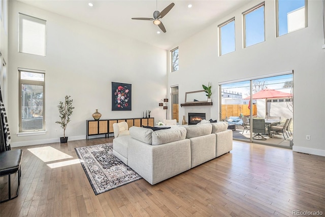 living area featuring a glass covered fireplace, baseboards, hardwood / wood-style floors, and recessed lighting