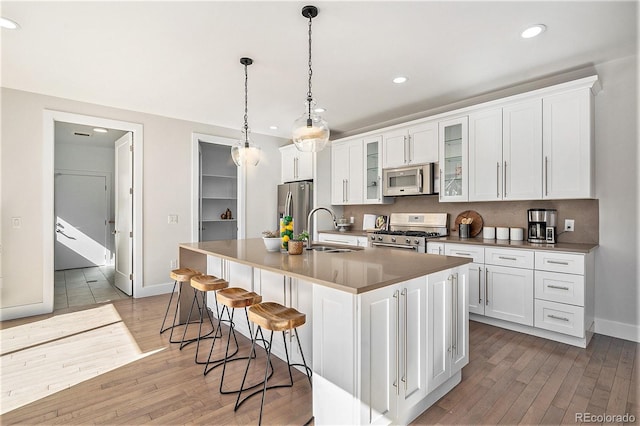 kitchen featuring light wood finished floors, appliances with stainless steel finishes, a kitchen island with sink, white cabinetry, and a sink