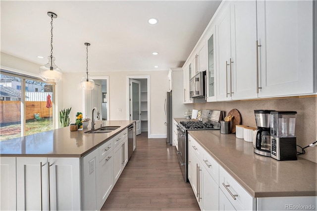 kitchen with stainless steel appliances, wood finished floors, a sink, white cabinets, and an island with sink