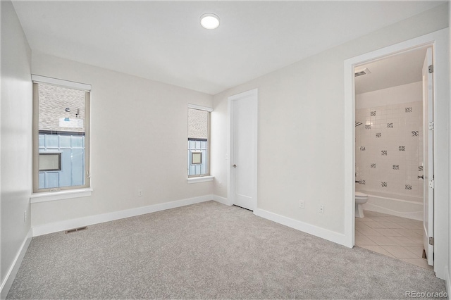 unfurnished bedroom with connected bathroom, tile patterned flooring, carpet flooring, visible vents, and baseboards