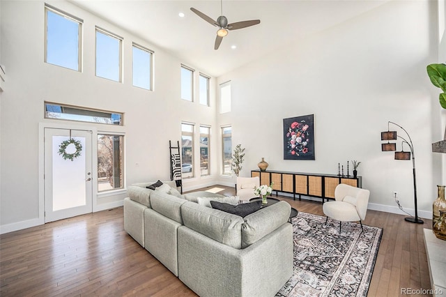 living area with baseboards, a high ceiling, hardwood / wood-style flooring, and ceiling fan