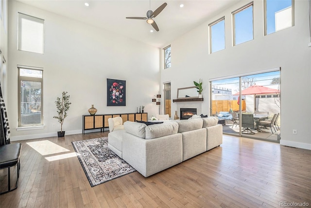 living area with a glass covered fireplace, ceiling fan, hardwood / wood-style flooring, and a towering ceiling