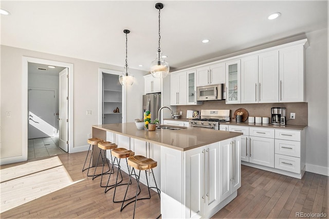 kitchen with a kitchen island with sink, a sink, stainless steel appliances, recessed lighting, and light wood-style flooring