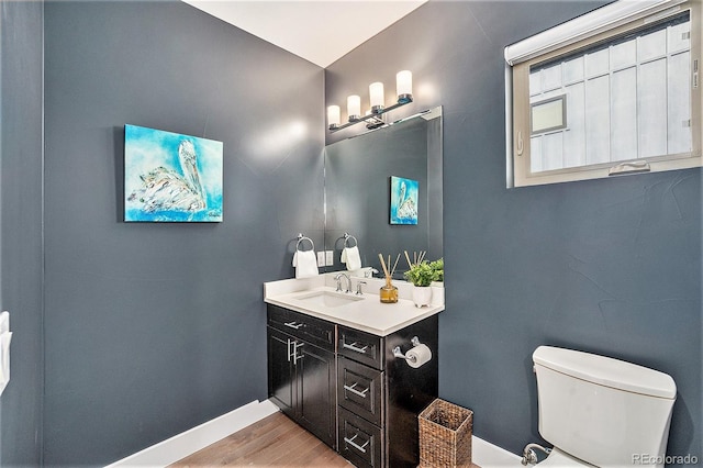 half bath featuring vanity, baseboards, toilet, and wood finished floors