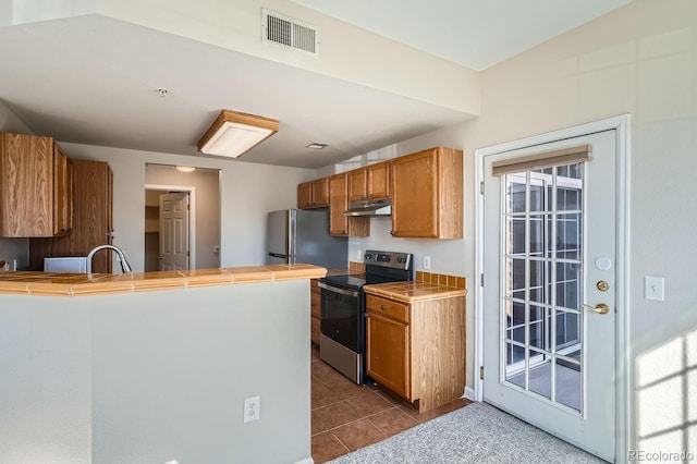 7440 S Blackhawk St Unit 4-102, Englewood, CO 80112 - kitchen with stainless steel appliances, tile counters, brown cabinetry, dark tile patterned floors, and under cabinet range hood