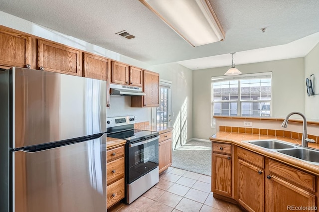 7440 S Blackhawk St Unit 4-102, Englewood, CO 80112 - kitchen with stainless steel appliances, a sink, under cabinet range hood, brown cabinetry, and a textured ceiling