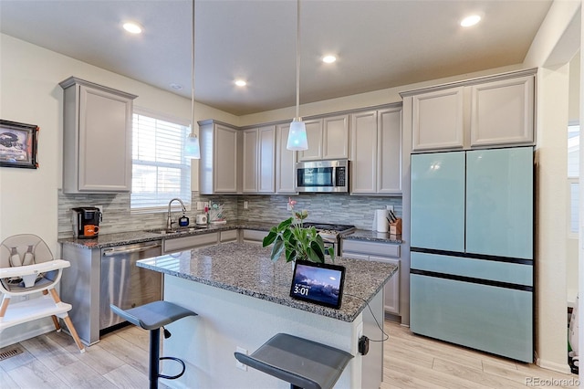 kitchen featuring sink, a center island, dark stone counters, a breakfast bar, and appliances with stainless steel finishes