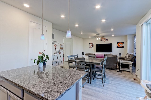 kitchen with stone counters, light hardwood / wood-style floors, hanging light fixtures, and ceiling fan