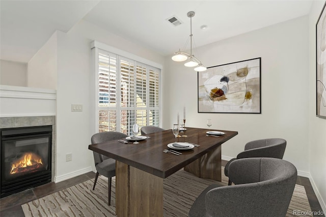 dining room featuring dark wood-type flooring, a fireplace, visible vents, and baseboards