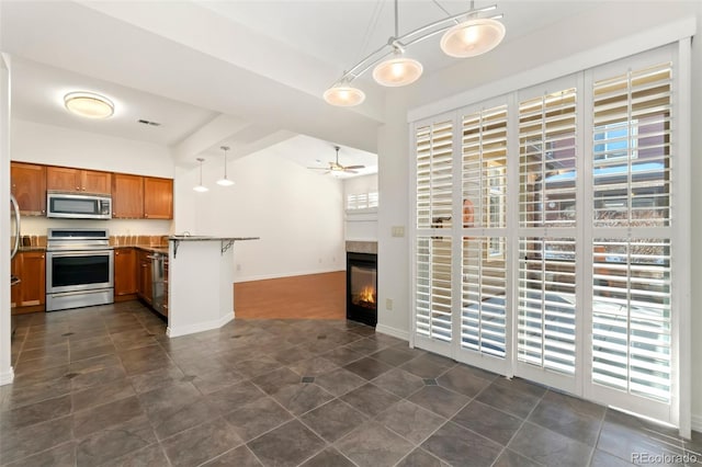 kitchen with brown cabinetry, a glass covered fireplace, appliances with stainless steel finishes, decorative light fixtures, and a peninsula