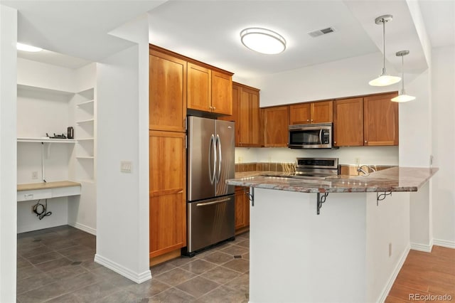 kitchen with a breakfast bar area, a peninsula, hanging light fixtures, appliances with stainless steel finishes, and brown cabinetry