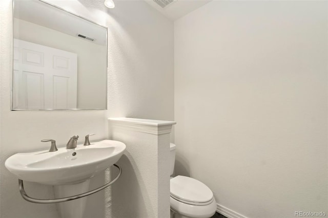 half bath featuring toilet, visible vents, and a sink