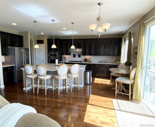 kitchen featuring decorative backsplash, decorative light fixtures, stainless steel appliances, and a center island with sink