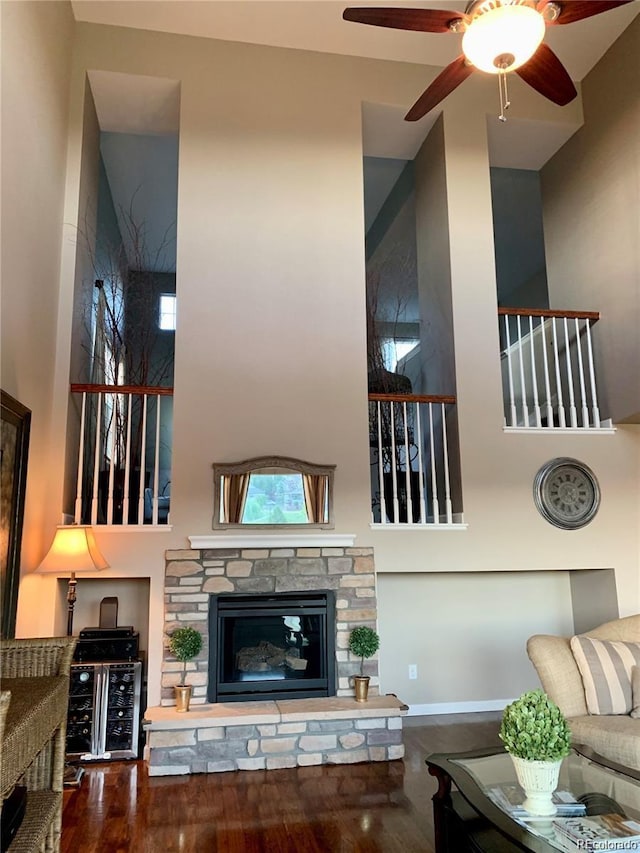 living room with hardwood / wood-style floors, ceiling fan, a towering ceiling, and a fireplace