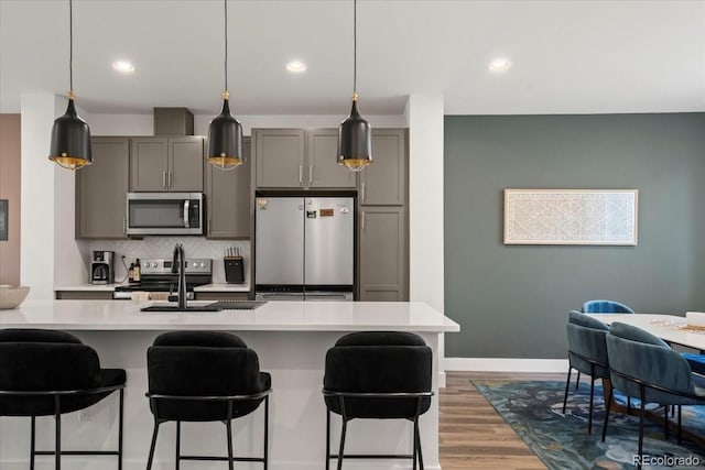 kitchen featuring stainless steel appliances, a breakfast bar, a sink, light countertops, and gray cabinets