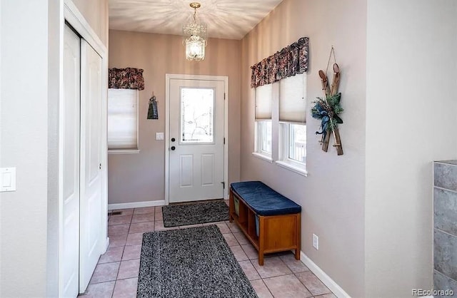 entryway featuring light tile patterned floors, a notable chandelier, and baseboards