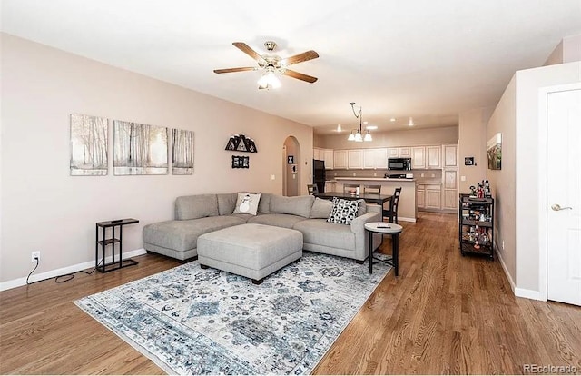 living room featuring ceiling fan with notable chandelier, arched walkways, baseboards, and wood finished floors