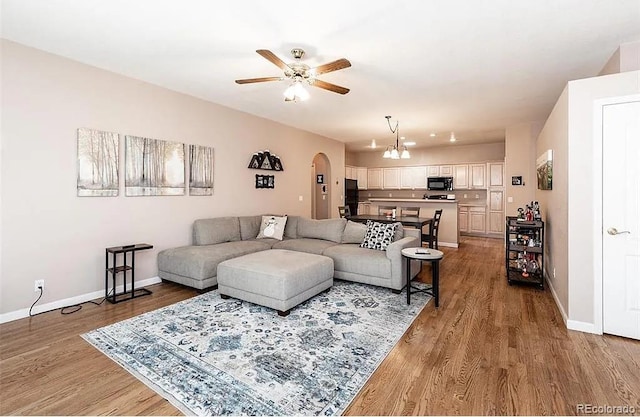 living area with arched walkways, ceiling fan with notable chandelier, wood finished floors, and baseboards