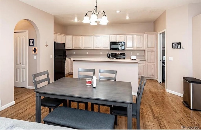 kitchen with arched walkways, pendant lighting, light countertops, light wood-style floors, and black appliances