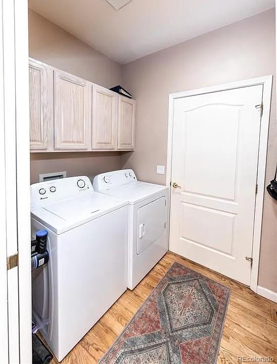 clothes washing area featuring light wood-type flooring, cabinet space, and independent washer and dryer