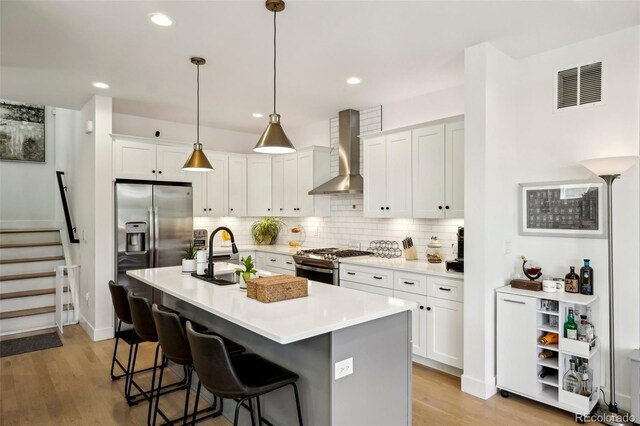 1299 Newton St, Denver, CO 80204 - kitchen with wall chimney exhaust hood, stainless steel appliances, tasteful backsplash, a sink, and light wood-type flooring