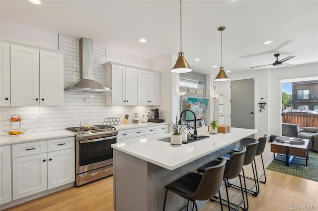 1299 Newton St, Denver, CO 80204 - kitchen with wall chimney range hood, stainless steel range with gas cooktop, a sink, backsplash, and light wood finished floors