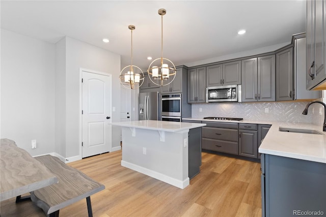 kitchen featuring gray cabinets, appliances with stainless steel finishes, a sink, an inviting chandelier, and light wood-style flooring