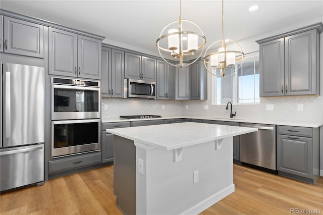 kitchen with gray cabinetry, appliances with stainless steel finishes, a sink, and a notable chandelier