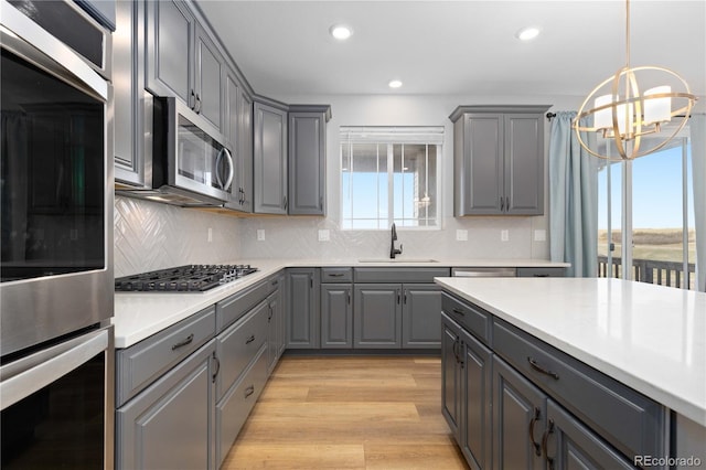 kitchen featuring stainless steel appliances, a sink, gray cabinets, and an inviting chandelier