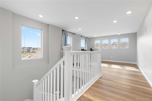 hall featuring a healthy amount of sunlight, recessed lighting, light wood finished floors, and an upstairs landing