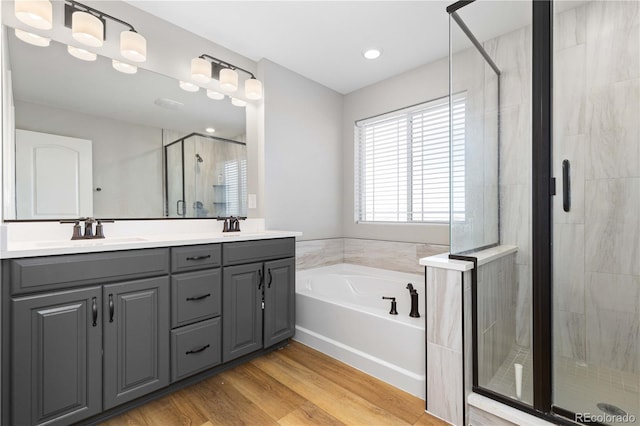 bathroom featuring double vanity, a bath, a shower stall, wood finished floors, and a sink