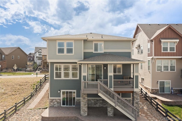 back of property featuring a residential view, fence, stone siding, and stairway