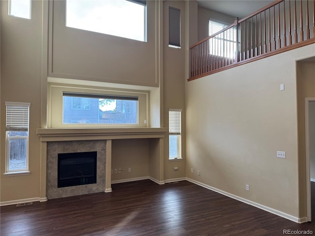 unfurnished living room with dark hardwood / wood-style flooring, a towering ceiling, and a tiled fireplace