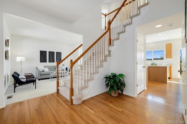 stairway with a towering ceiling, visible vents, wood finished floors, and recessed lighting