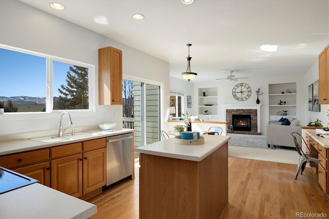 kitchen featuring light wood finished floors, light countertops, a brick fireplace, a kitchen island, and dishwasher