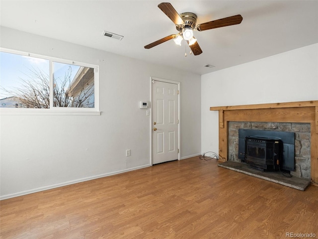 unfurnished living room with light wood-type flooring, ceiling fan, and a wood stove