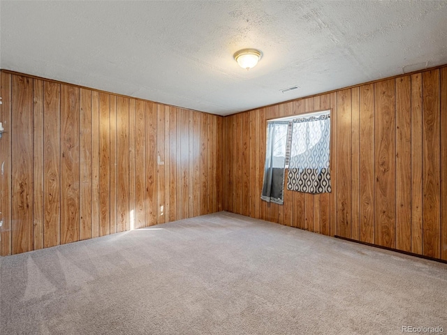 empty room with a textured ceiling, wooden walls, and light carpet