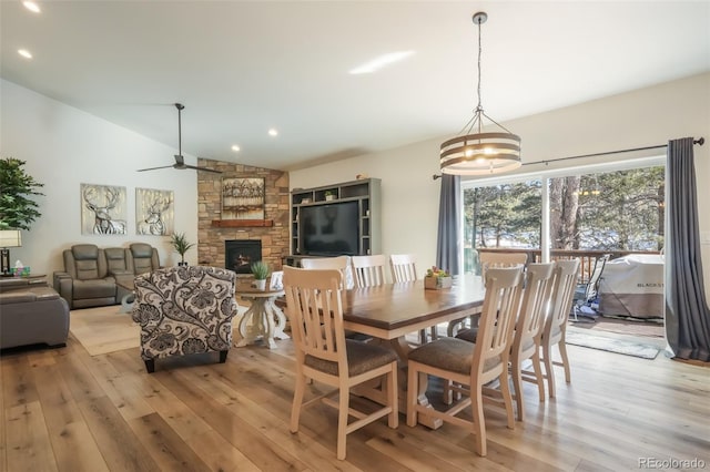 dining room featuring ceiling fan, lofted ceiling, a fireplace, and light hardwood / wood-style floors