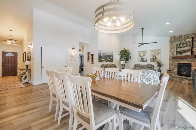 dining space with a towering ceiling, a fireplace, ceiling fan with notable chandelier, and light wood-type flooring