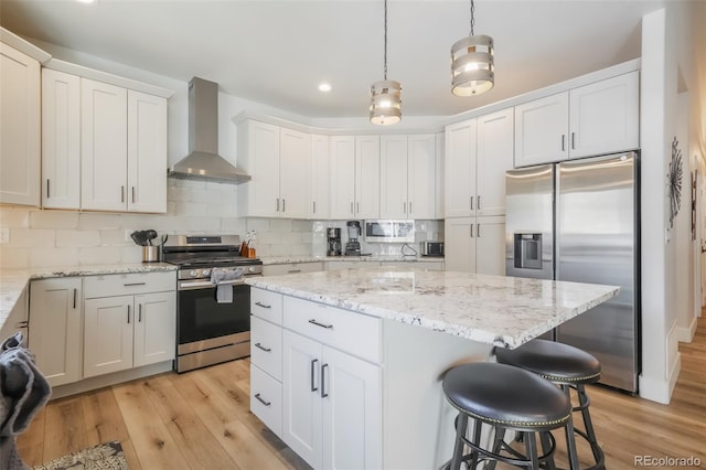 kitchen with backsplash, appliances with stainless steel finishes, pendant lighting, wall chimney range hood, and white cabinets