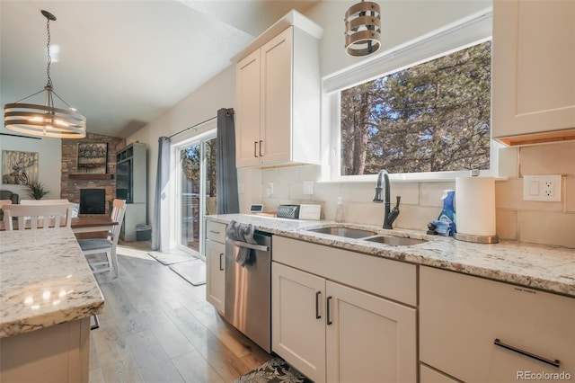 kitchen with sink, dishwasher, light stone counters, a fireplace, and decorative backsplash