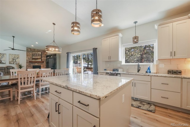 kitchen featuring a stone fireplace, sink, hanging light fixtures, a kitchen island, and backsplash