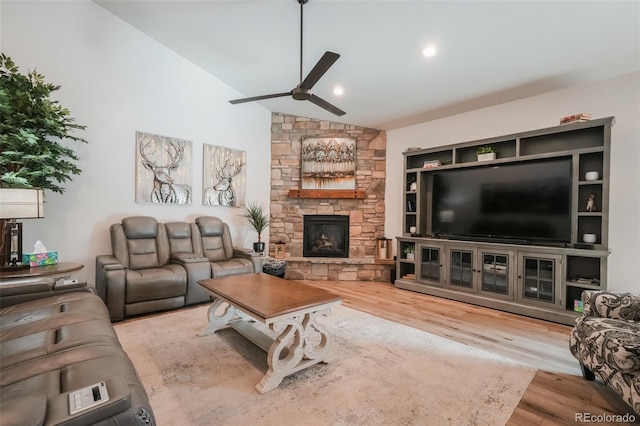 living room with vaulted ceiling, ceiling fan, a stone fireplace, and hardwood / wood-style floors