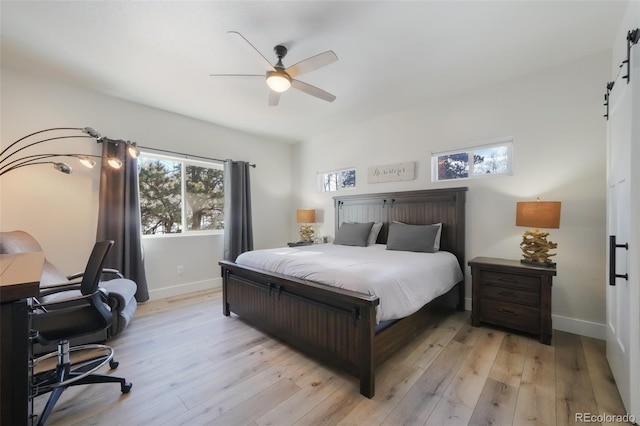 bedroom with a barn door, ceiling fan, and light hardwood / wood-style flooring