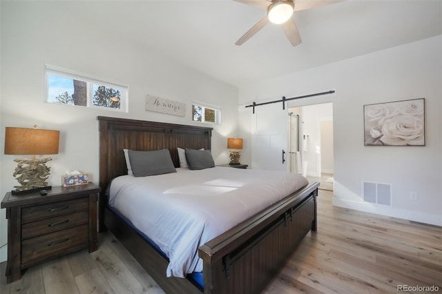 bedroom with ceiling fan, a barn door, and light wood-type flooring