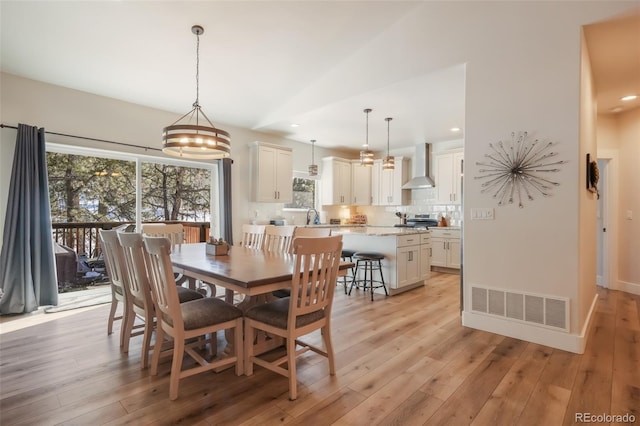 dining room featuring sink, light hardwood / wood-style flooring, and vaulted ceiling