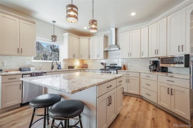 kitchen featuring appliances with stainless steel finishes, decorative light fixtures, sink, a center island, and wall chimney range hood